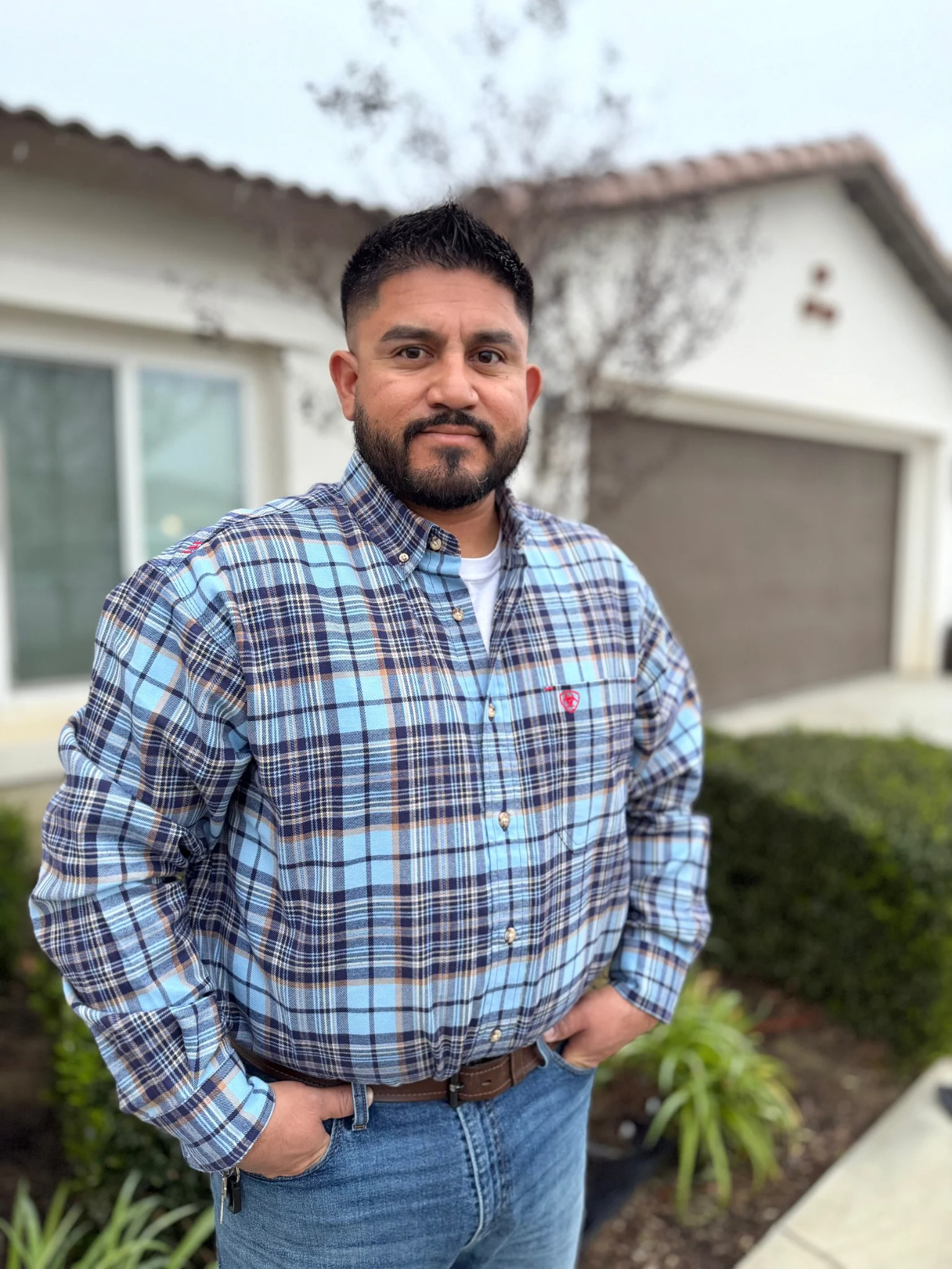 OTG Concrete owner in blue plaid shirt standing in front of residential house with garage and landscaping