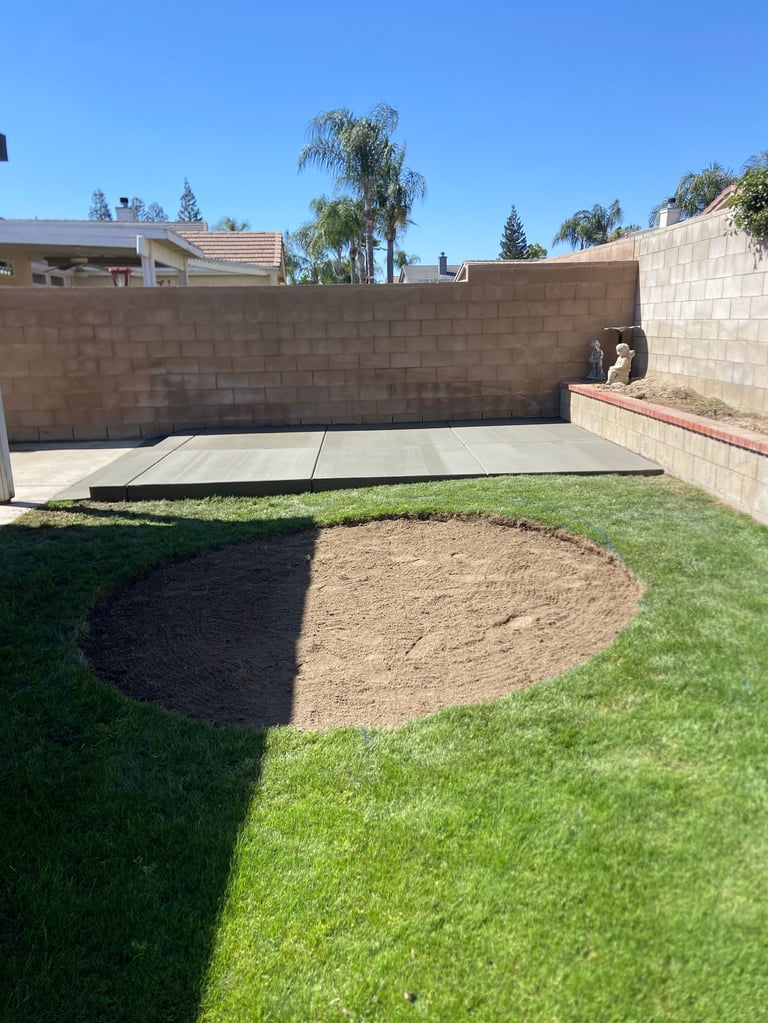 Sunny backyard with manicured lawn, concrete patio, stone walls, and landscaping under clear blue sky