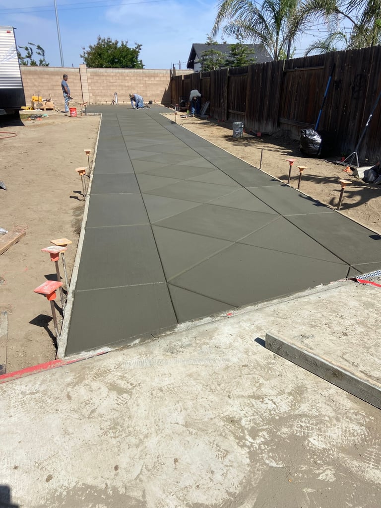 Concrete pathway being poured in a residential backyard with wooden fences and marker stakes along the sides