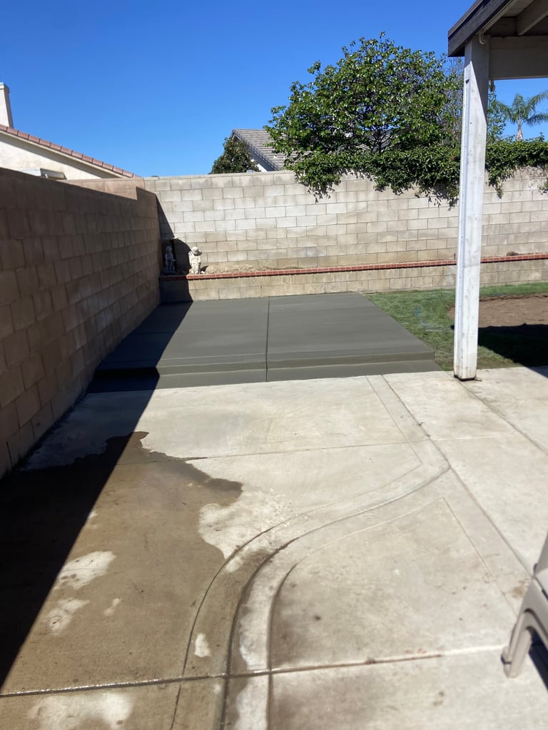Concrete driveway with dark green cover over part of the surface, bounded by cinder block walls and white support post