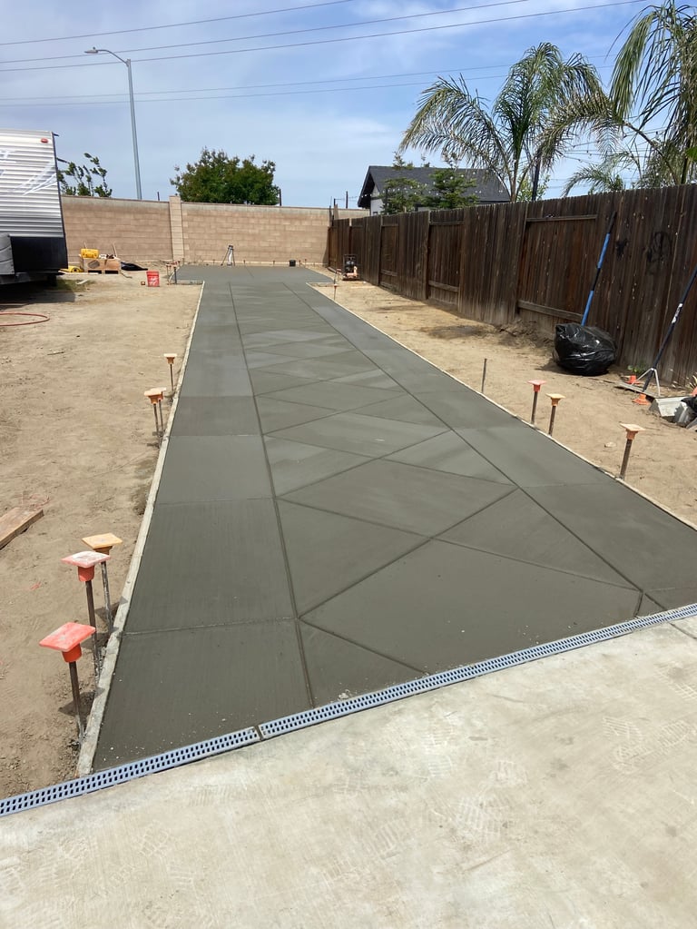 Newly poured concrete pathway in backyard construction with wooden fences and palm trees visible in background